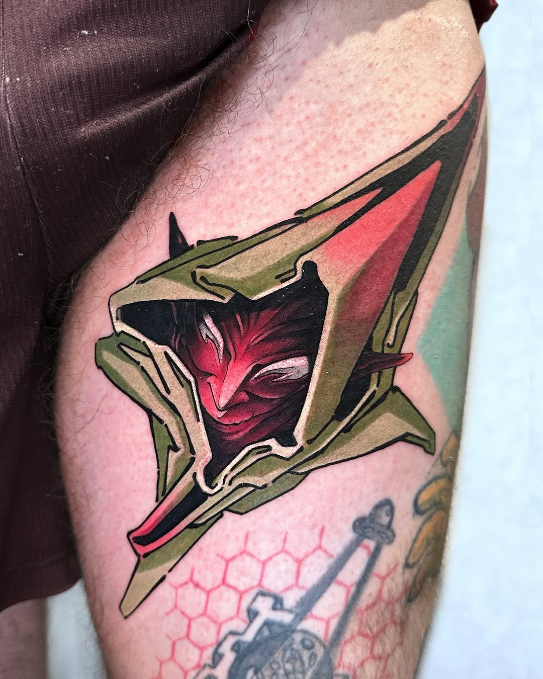 Colorful flower tattoo on thigh featuring red petals and green leaves with black outlines and shading.