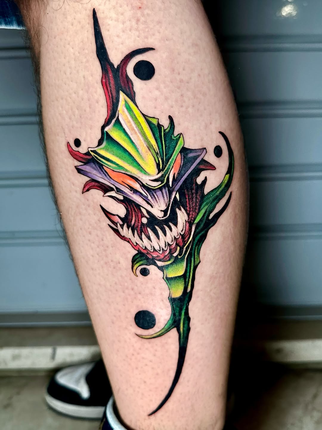 Colorful skull with horns and floral elements on a green stem, featuring yellow, red, purple, and green colors, tattooed on the calf.