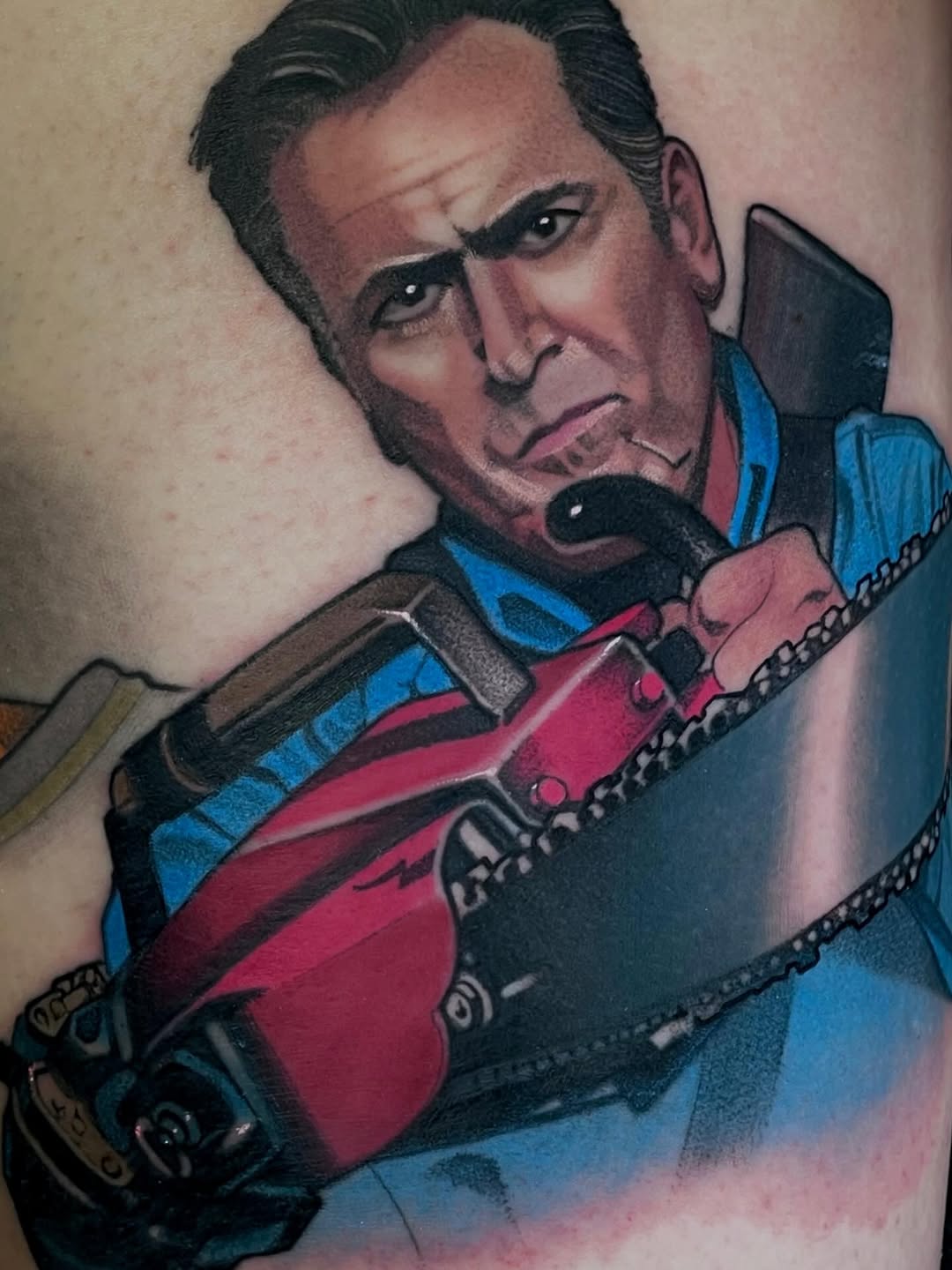 Colorful shoulder tattoo depicting a man with dark hair holding a red guitar, wearing a blue jacket with chain details.