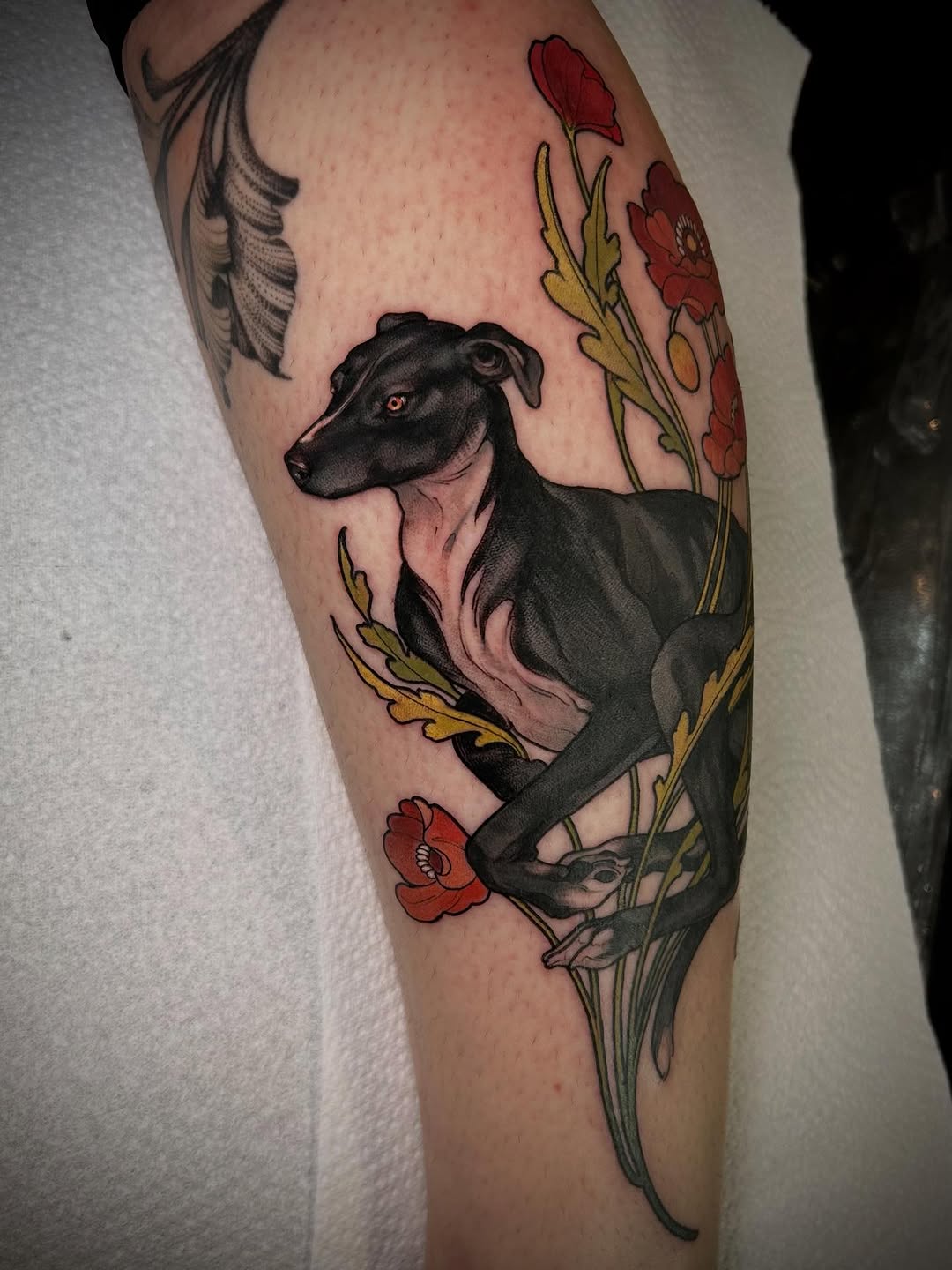 Black dog with pink tongue and red eyes surrounded by red and yellow flowers on the upper leg.