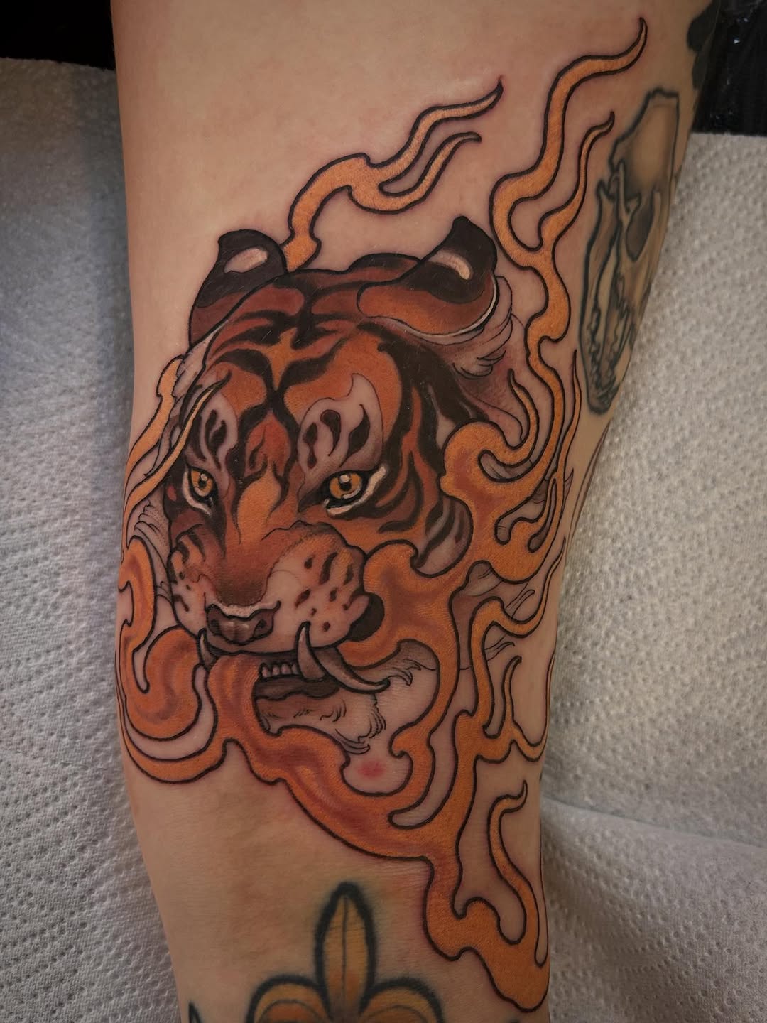 Tiger head surrounded by flowing flames in orange, red, and black ink on the inner thigh.