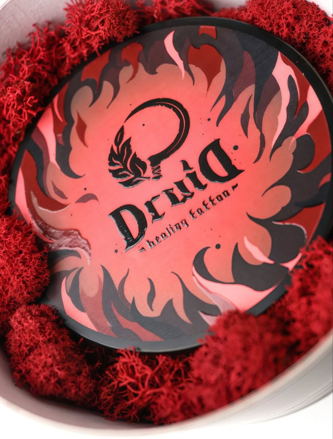 Skull with floral eye and "Denim" text surrounded by flame design in red and black on circular background with red textured border.