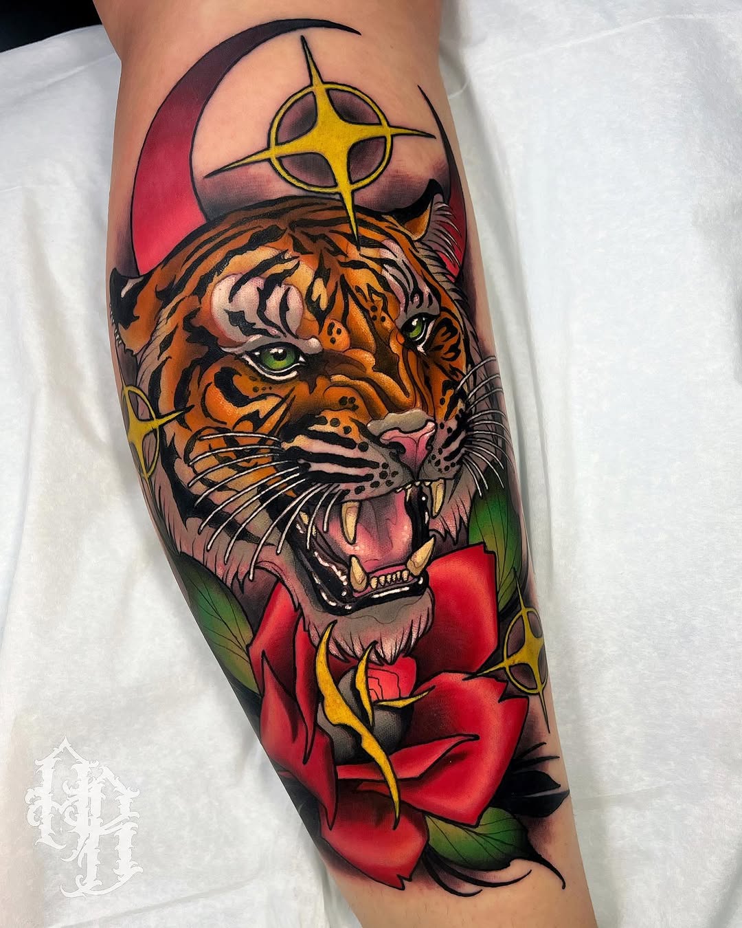 Tiger head with open mouth and green eyes wearing a crescent moon and four-pointed star, surrounded by red roses with green leaves on a calf.