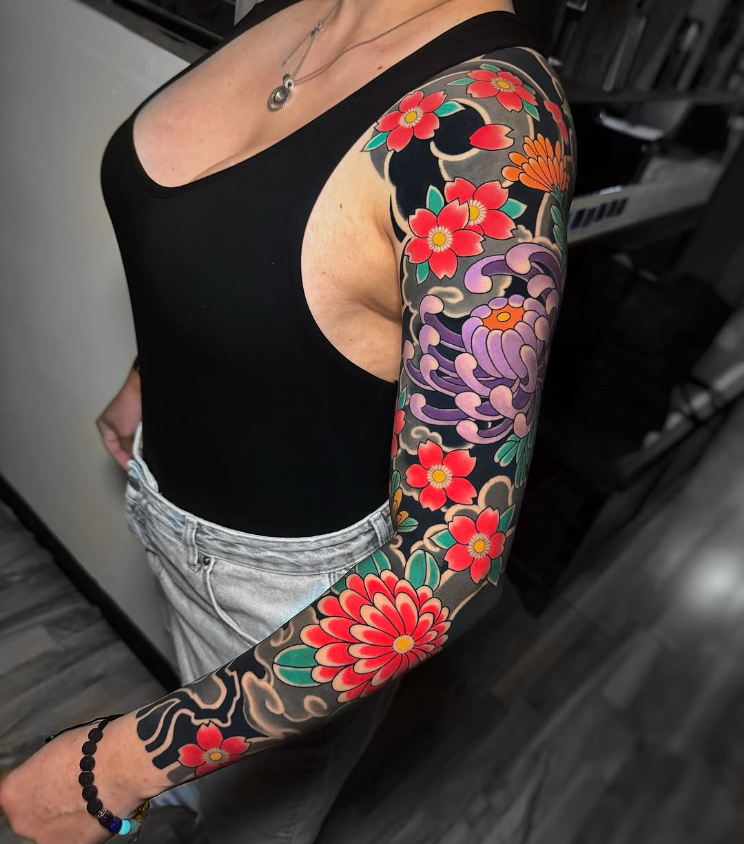 Full-sleeve arm tattoo featuring red and purple flowers with green leaves and ornamental black designs on a tan background.
