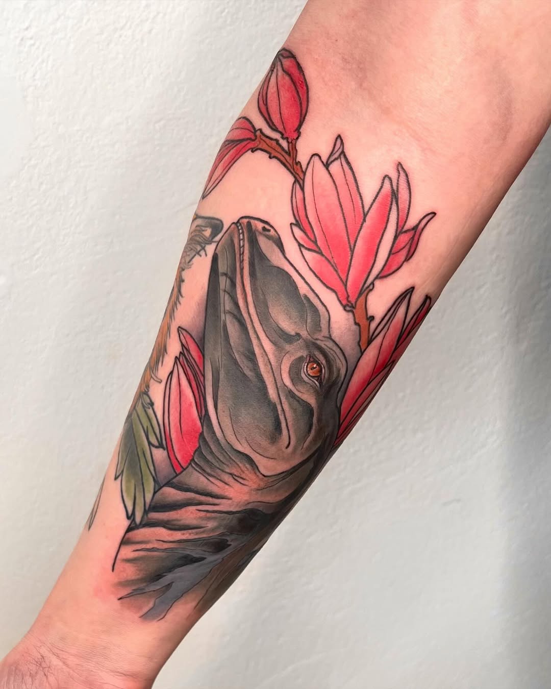 Hippopotamus head with orange eye surrounded by red flower buds on forearm, rendered in gray and red ink.