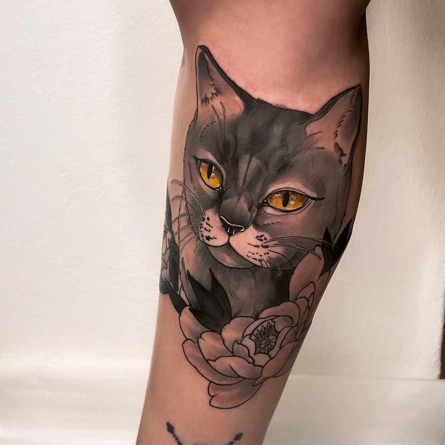 Black cat with golden yellow eyes and pink nose on calf, accompanied by a pink flower with detailed petals below.