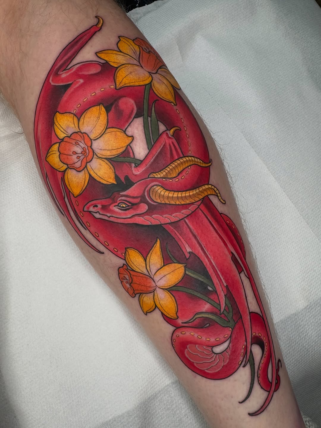 Red chili pepper tattoo with yellow flowers and green stems on a calf, featuring decorative dotted lines and detailed shading in warm tones.