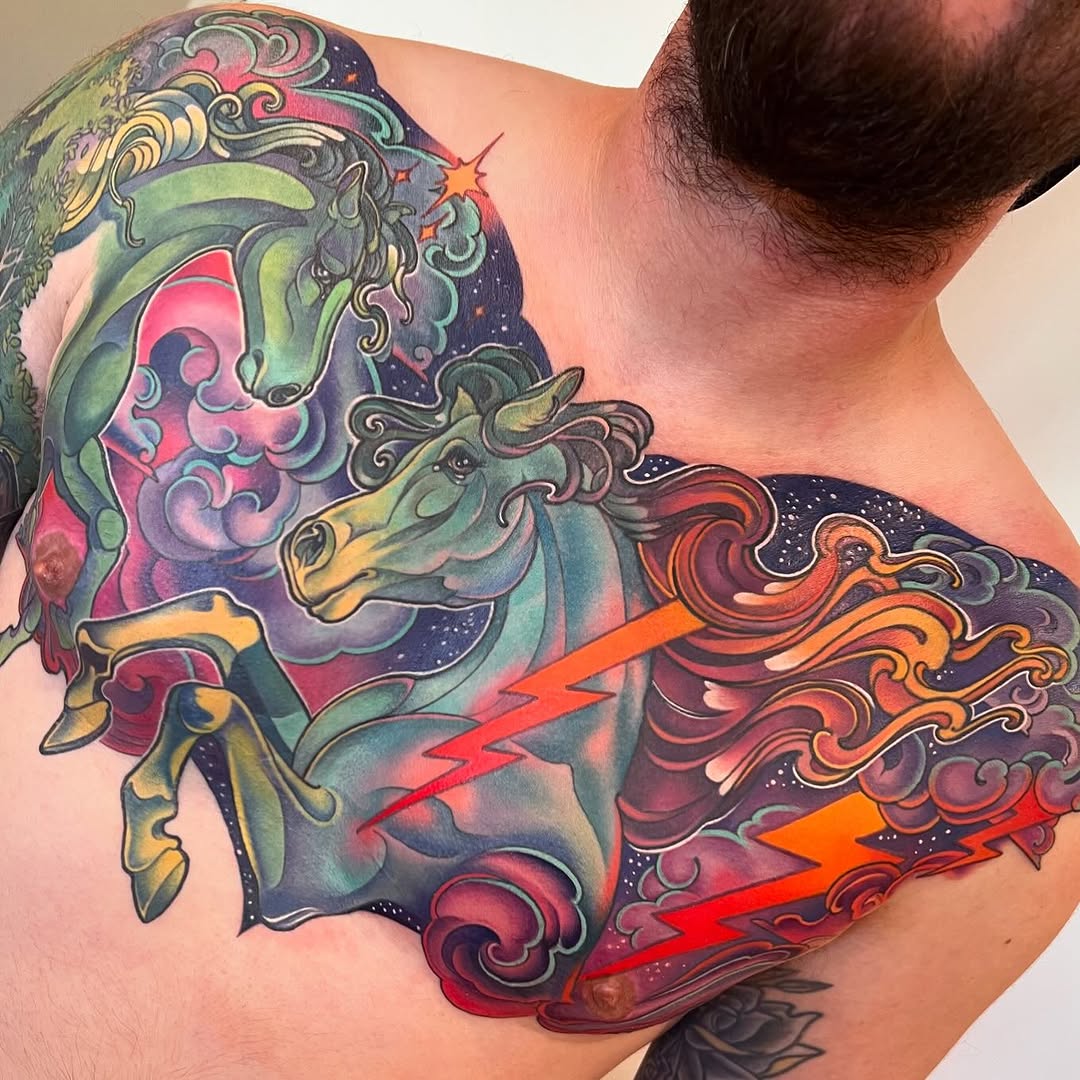 Colorful shoulder tattoo featuring two ornate horse heads with decorative scrollwork, lightning bolts, and cosmic elements in vibrant blues, purples, reds, and golds.