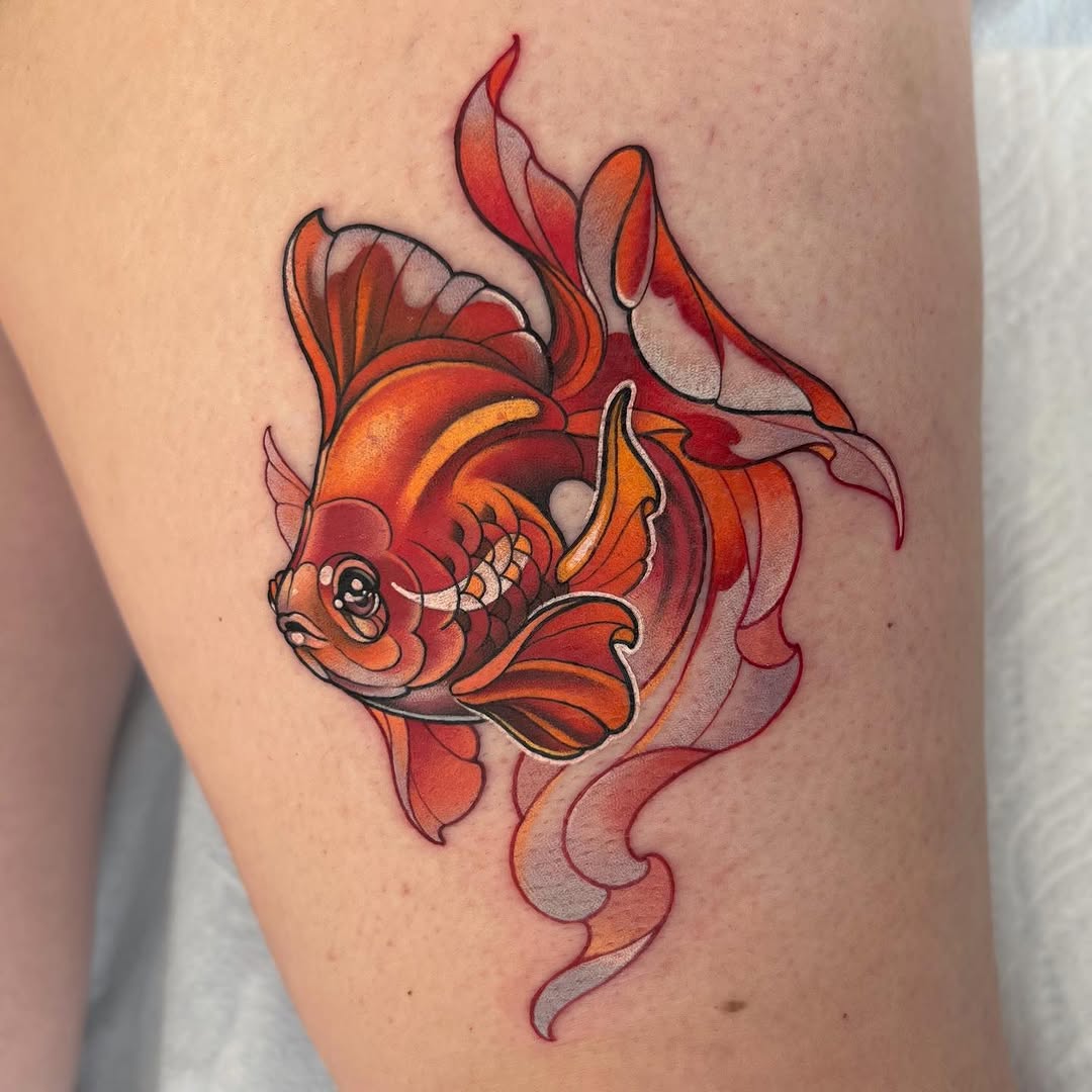 Colorful goldfish tattoo with flowing fins in shades of red, orange, and yellow on the upper arm, featuring detailed scales and a prominent eye.