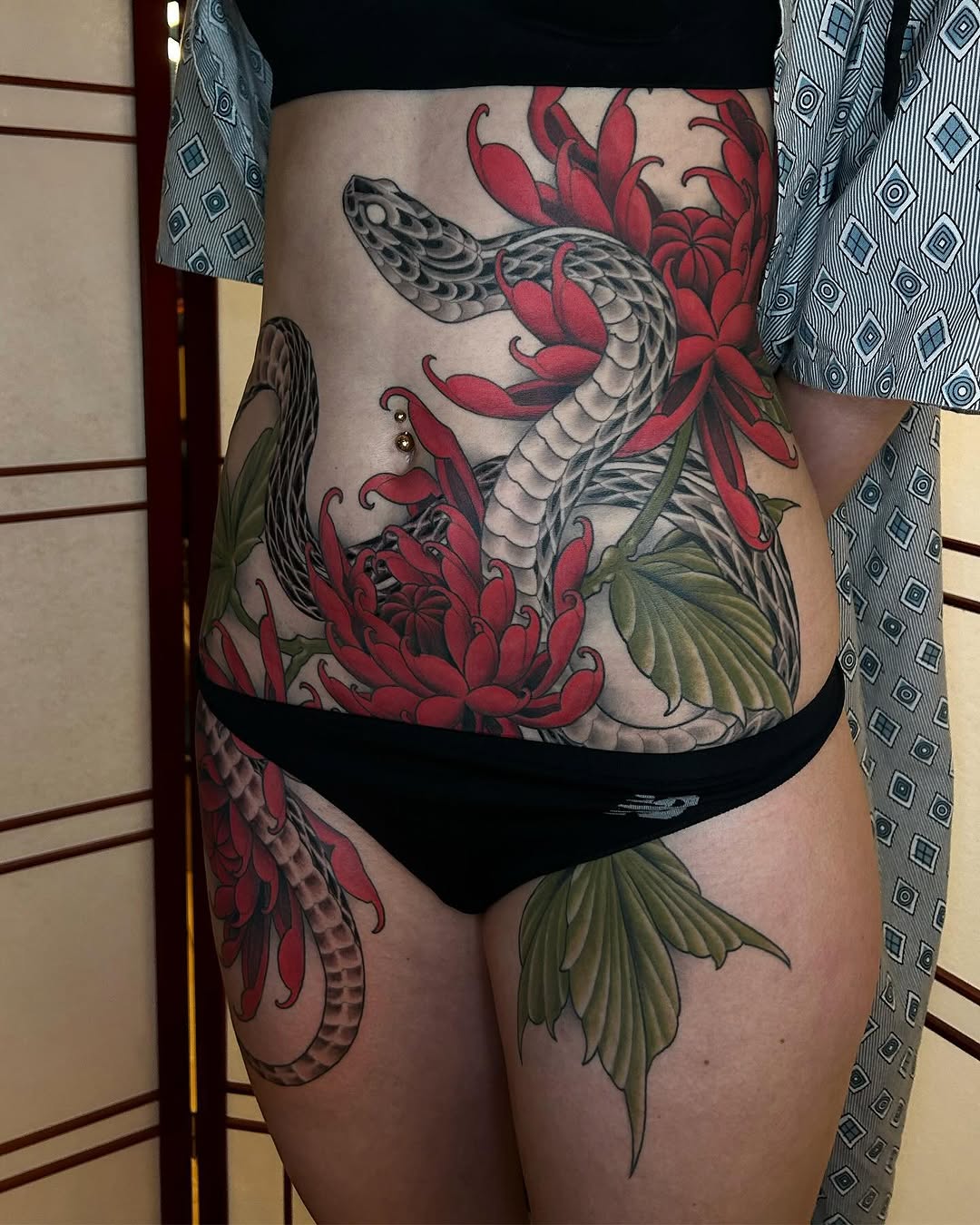 Colorful dragon and red lotus flower tattoo with green leaves on torso and thigh in red, black, and green ink.