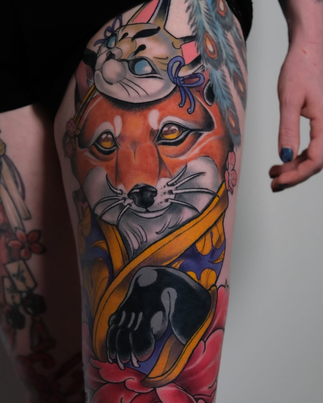 Colorful leg tattoo featuring stacked cat faces with orange, blue, and yellow clothing elements, flowers, and decorative details on the thigh and calf.