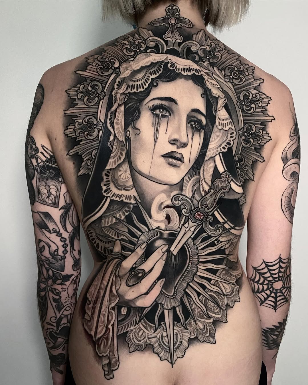 Back tattoo featuring a woman's portrait with ornate decorative elements, tears, and intricate linework in black ink on pale skin.