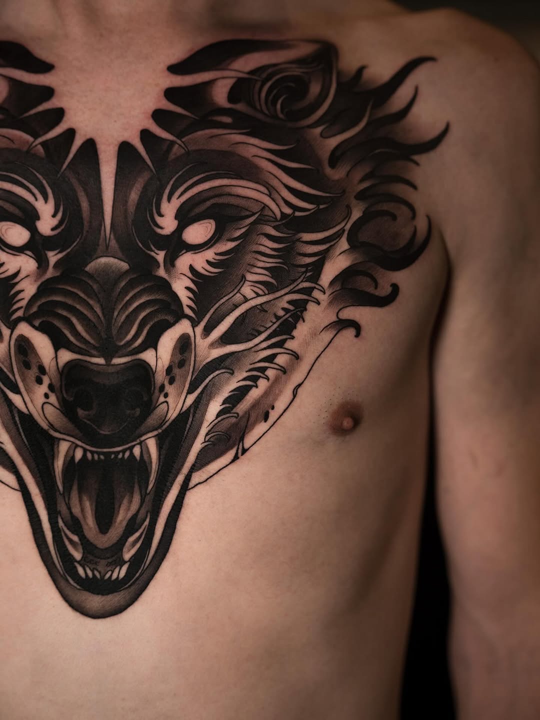 Large ornate demon or beast head tattoo with flowing decorative elements covering the chest and shoulder in black ink.