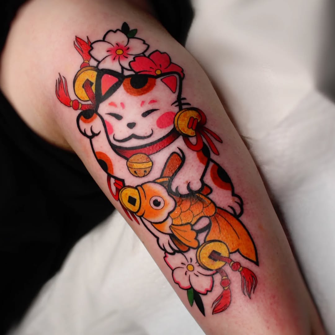 Colorful arm tattoo featuring a smiling cat with flowers and gold coins above an orange koi fish surrounded by pink flowers and red leaves.