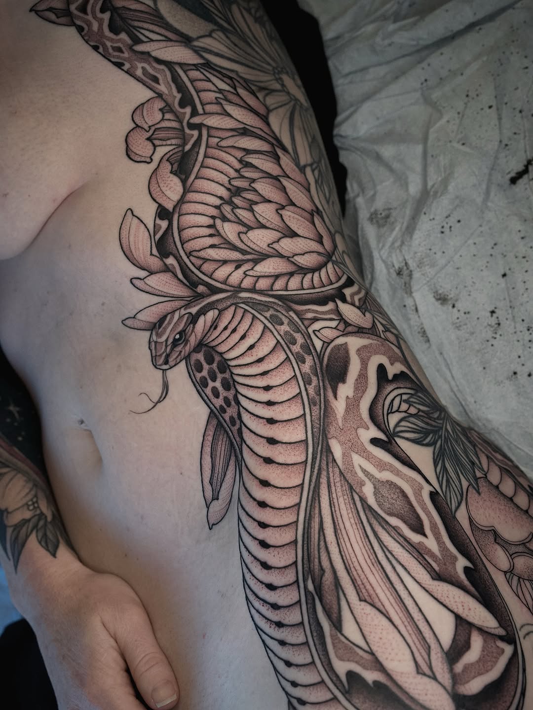 Detailed bee and floral sleeve tattoo featuring layered wings, botanical elements, and dotwork shading in black and brown ink on the upper arm.