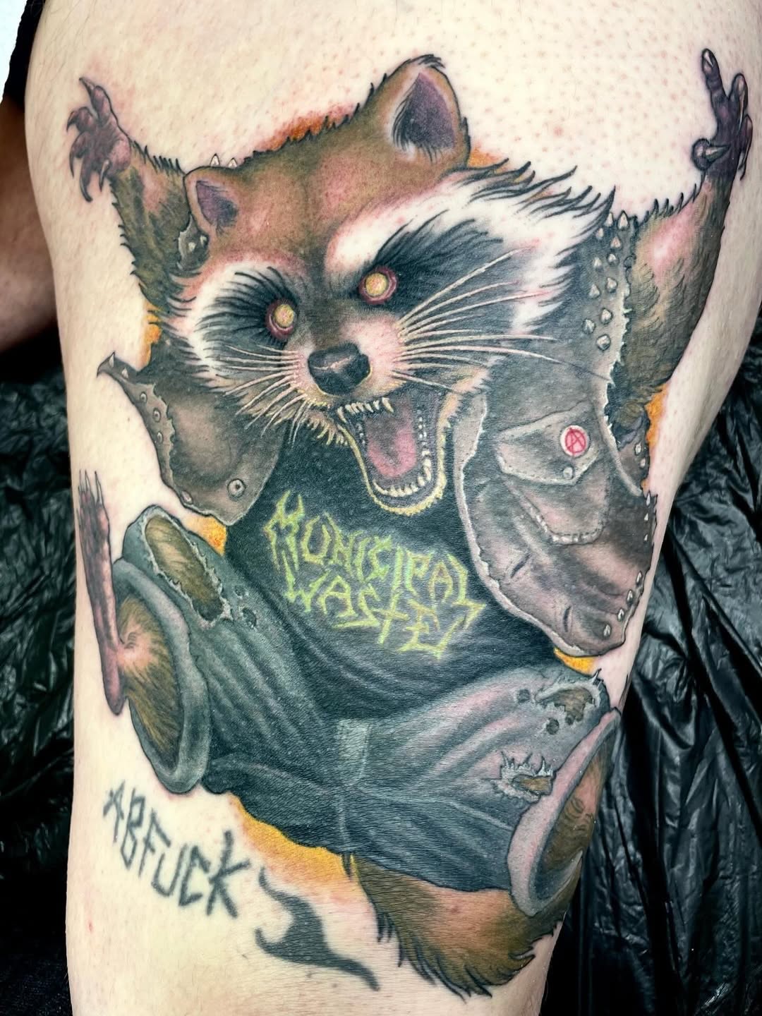 Anthropomorphic raccoon character wearing studded leather jacket and band t-shirt on upper arm, rendered in color with yellow eyes and text details.