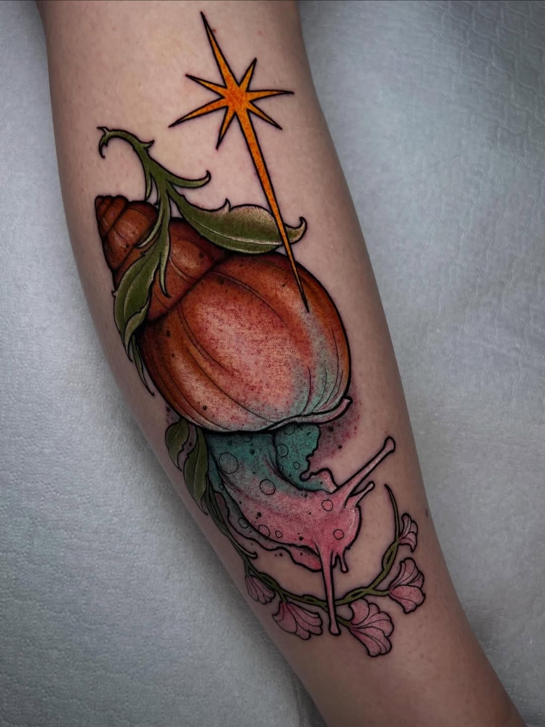 Colorful strawberry tattoo on forearm featuring red fruit, green leaves, pink flower, star, and detailed shading in orange, green, and pink tones.