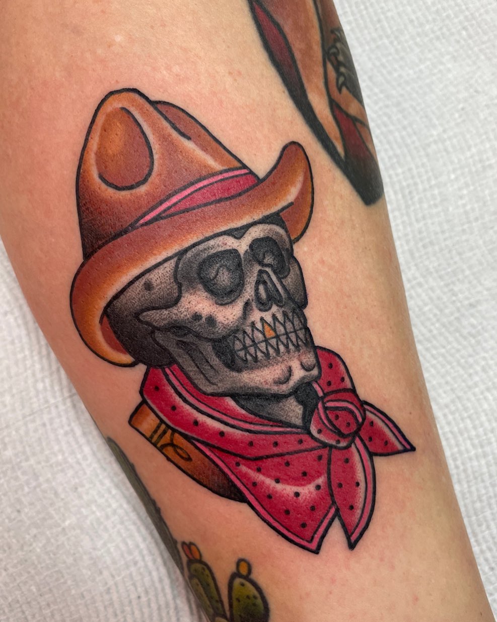 Colored skull wearing a red bandana and orange cowboy hat on an upper arm, with black outline details.
