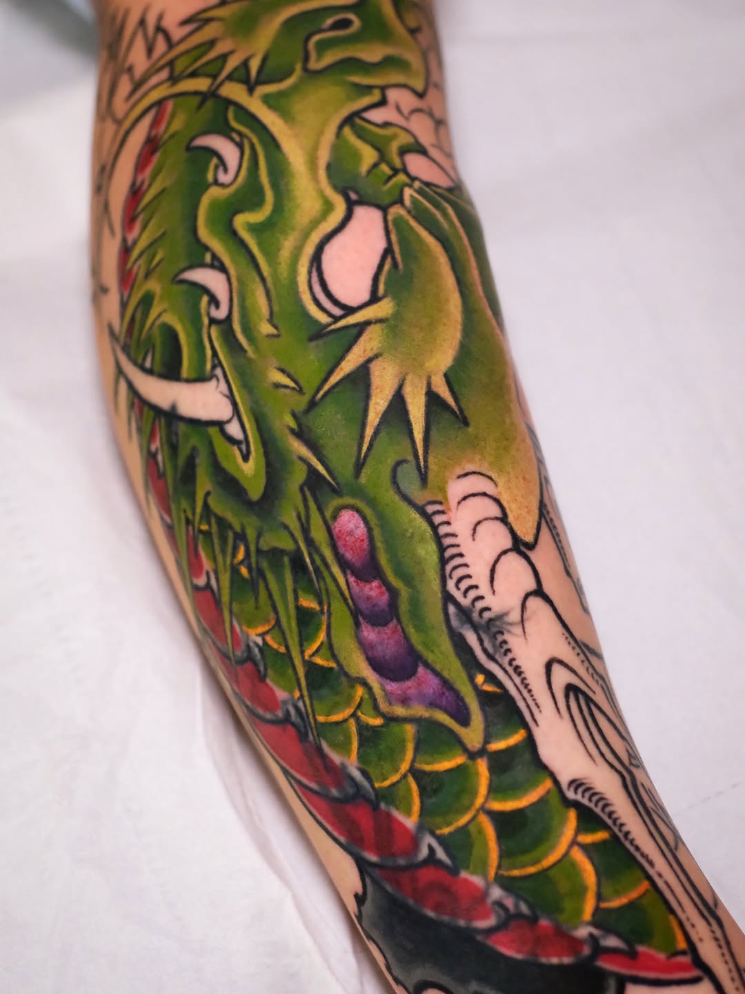 Colorful dragon tattoo on forearm featuring green scales, red accents, yellow details, and white facial features with open mouth.