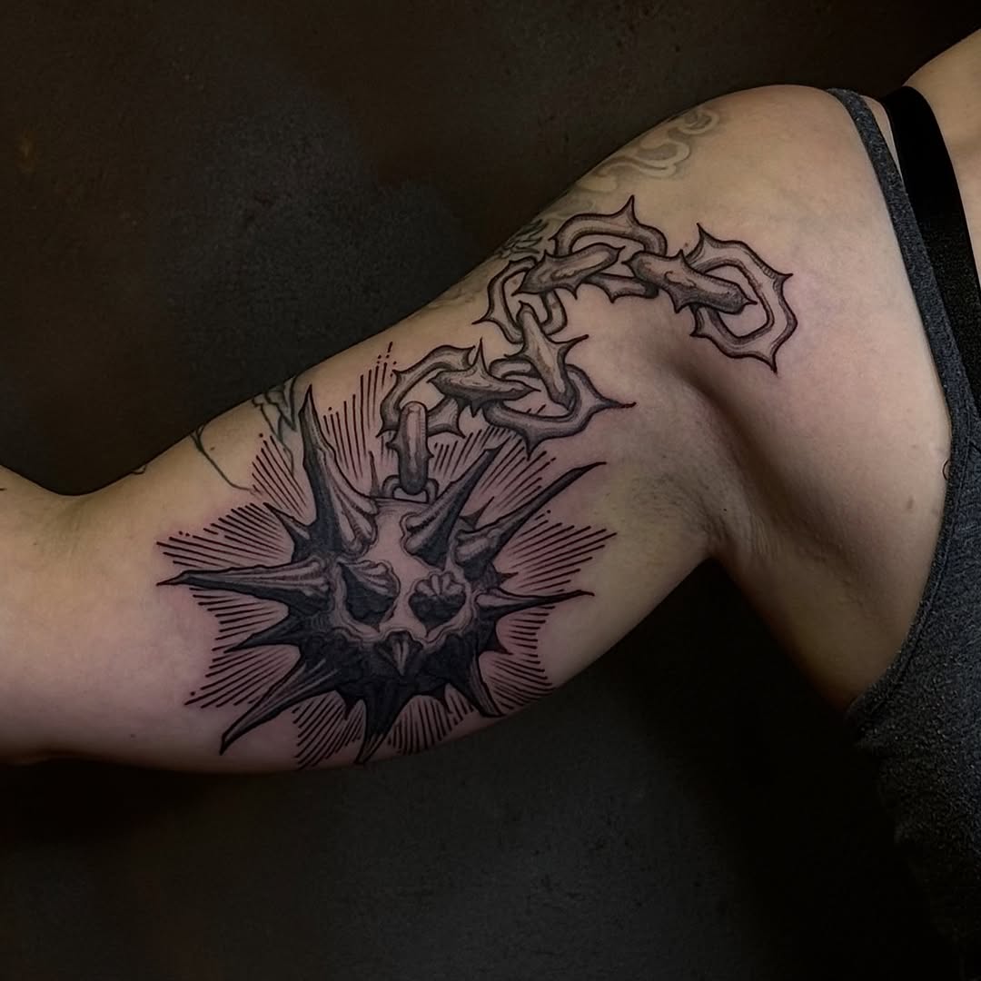 Detailed black ink tattoo on upper arm featuring a spiky creature head with tentacle-like appendages extending upward.