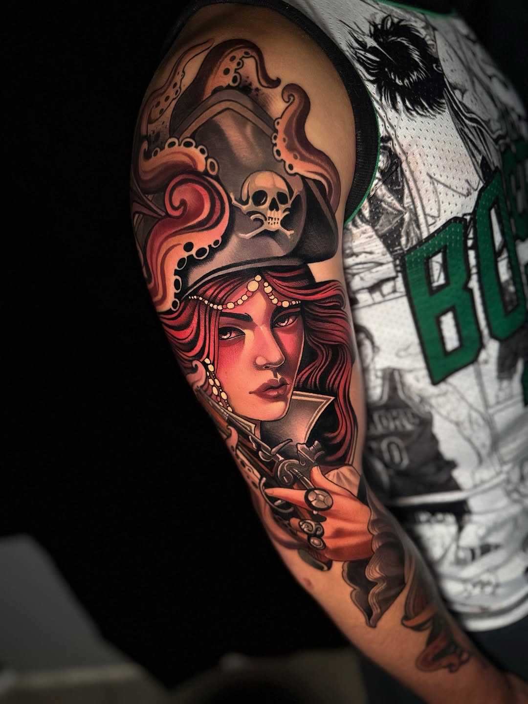 Large shoulder and upper arm tattoo featuring a woman's portrait in red and orange tones with ornate headdress, skull imagery, and decorative scrollwork elements.