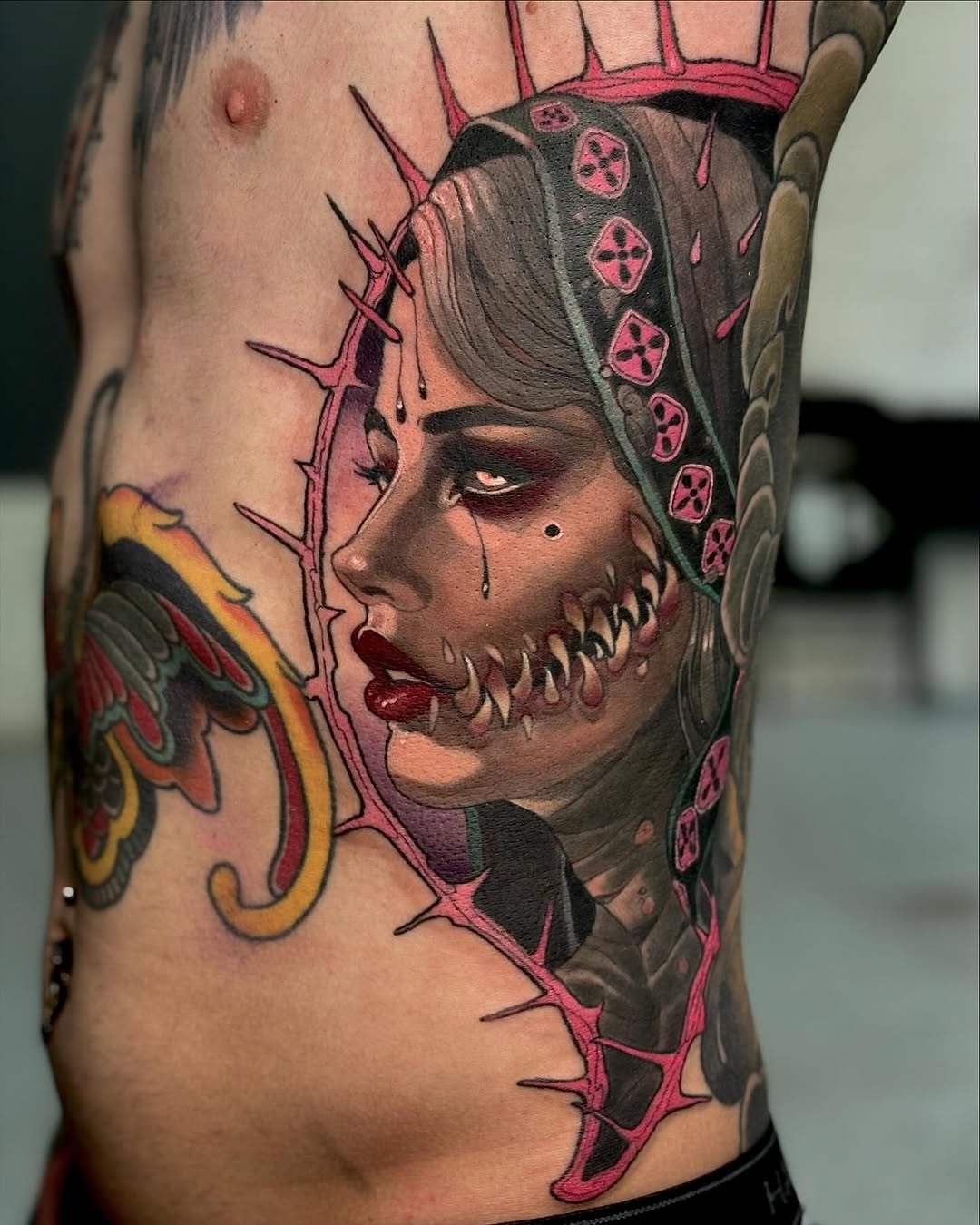 Colored tattoo on ribs featuring a female face with skull makeup, thorned crown, and pink geometric patterns on the headdress.