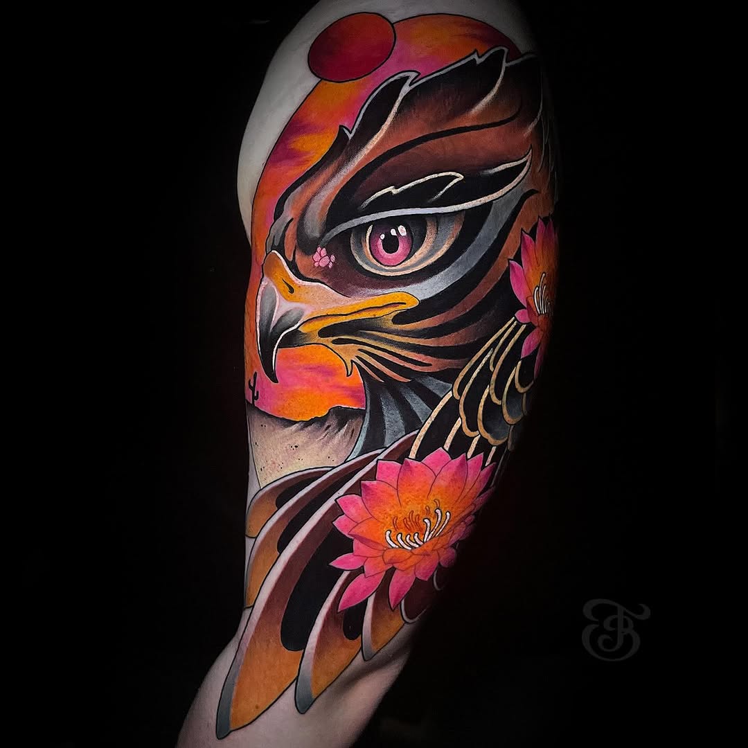Colorful eagle head tattoo on upper arm featuring pink eye, orange and black shading, pink lotus flowers, and warm sunset tones.