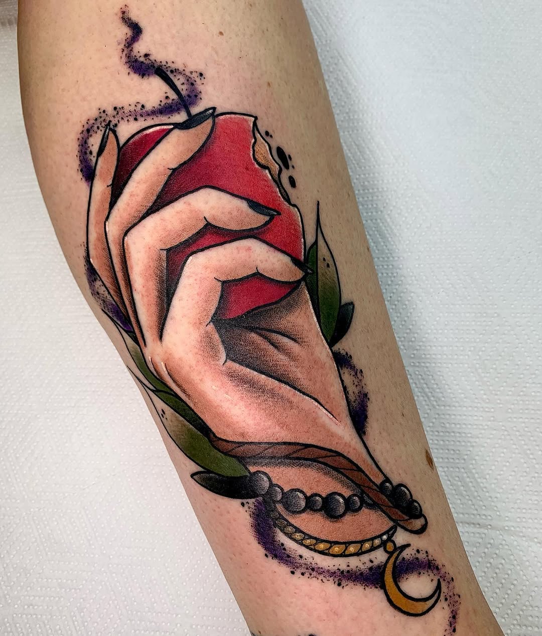 Hand holding a red apple with purple sparkles, green leaves, and decorative beaded bracelets on the forearm, featuring a crescent moon charm.