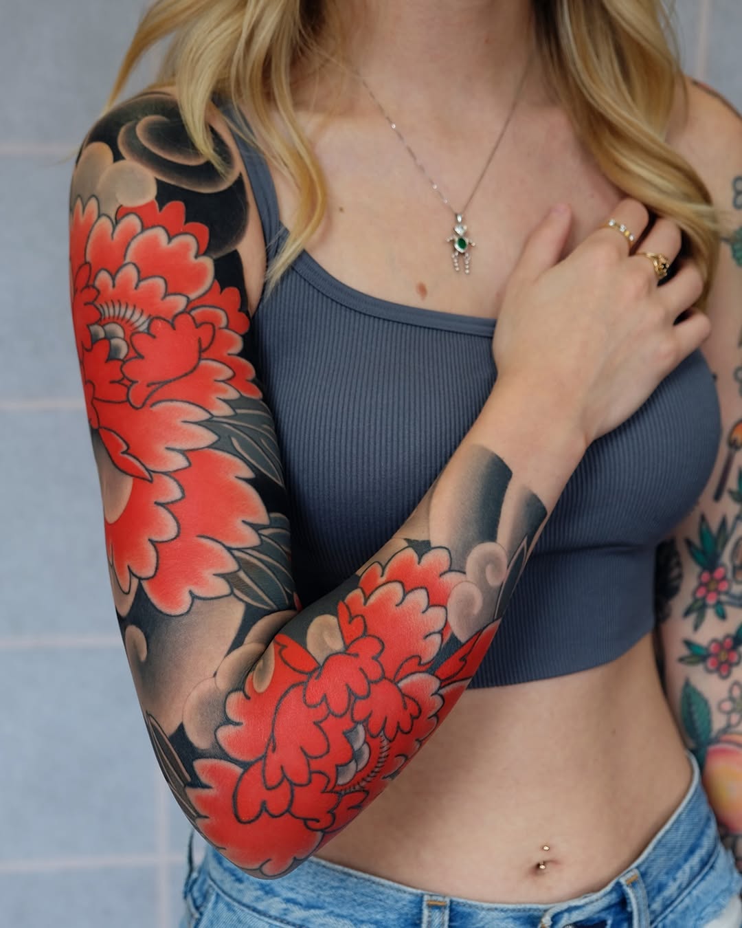 Woman displaying a full-sleeve arm tattoo featuring large red flowers with dark shading and botanical elements on her right arm.