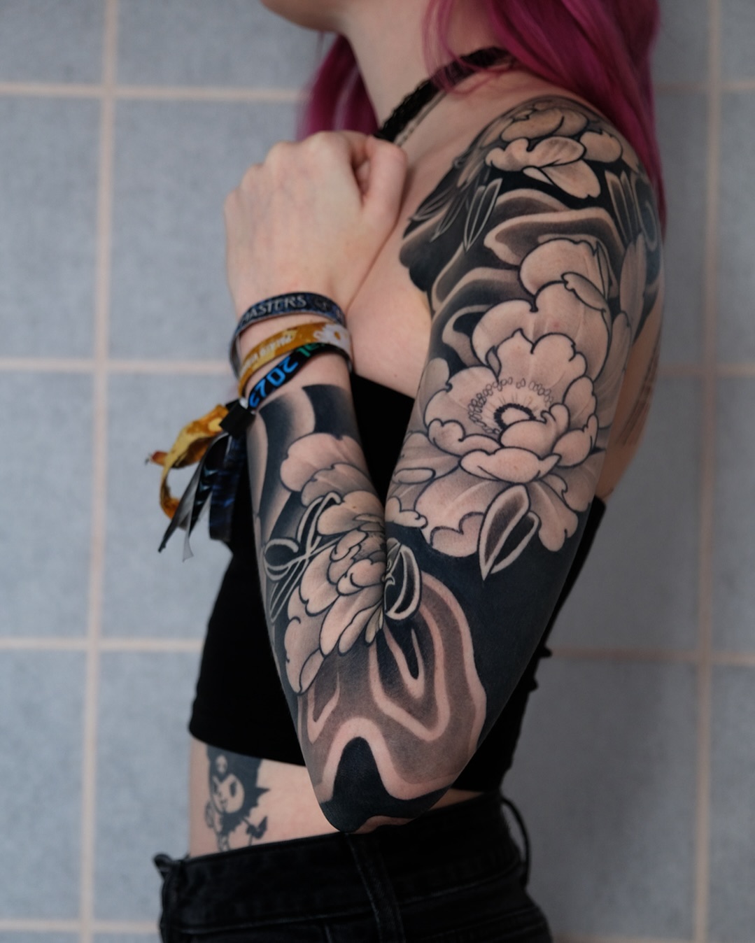 Large-scale floral sleeve tattoo in black and gray featuring layered peonies on the upper arm and shoulder of a person wearing a black tank top.