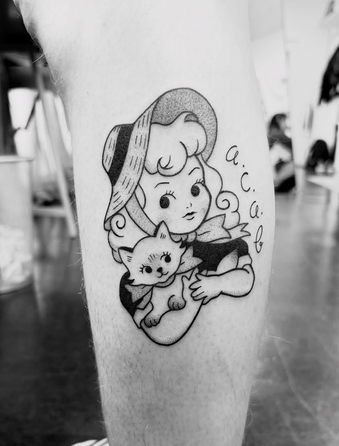 Vintage-inspired tattoo on thigh featuring a woman in a hat holding a smiling cat, with decorative lettering, rendered in black ink.