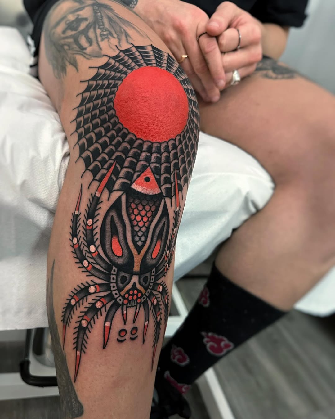 Large-scale bird tattoo on thigh featuring black linework with red and orange accents, centered red circle, and ornate feather details below.