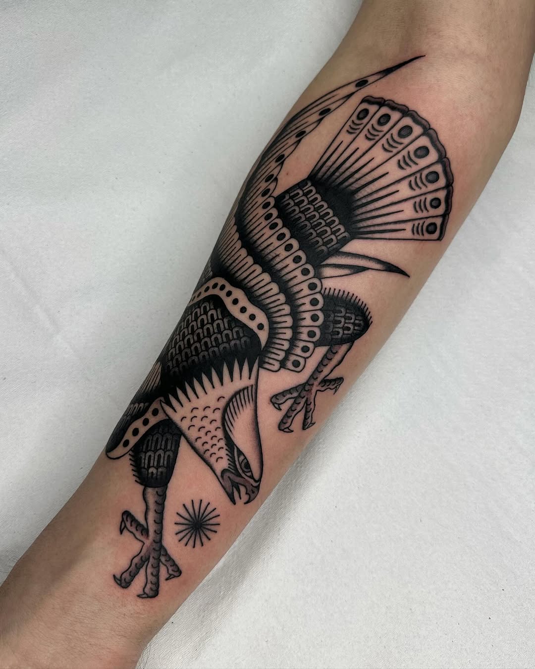 Detailed bird tattoo on forearm featuring layered wings, geometric patterns, decorative elements, and fine linework in black ink.