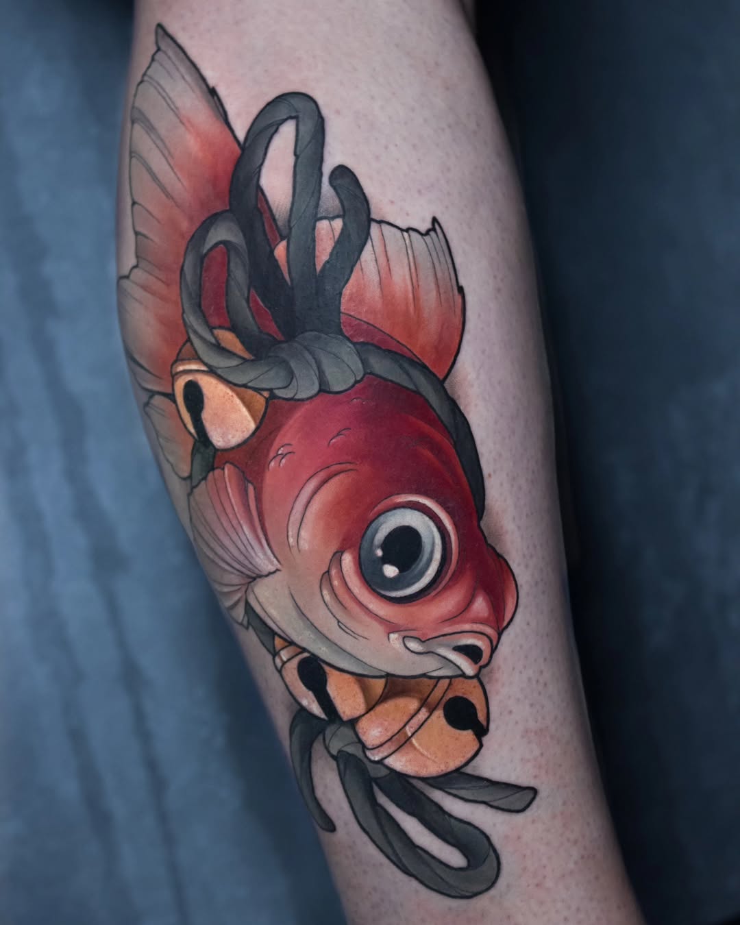 Colorful fish head tattoo with red, orange, and black details on an upper arm, featuring prominent eyes and flowing fins.