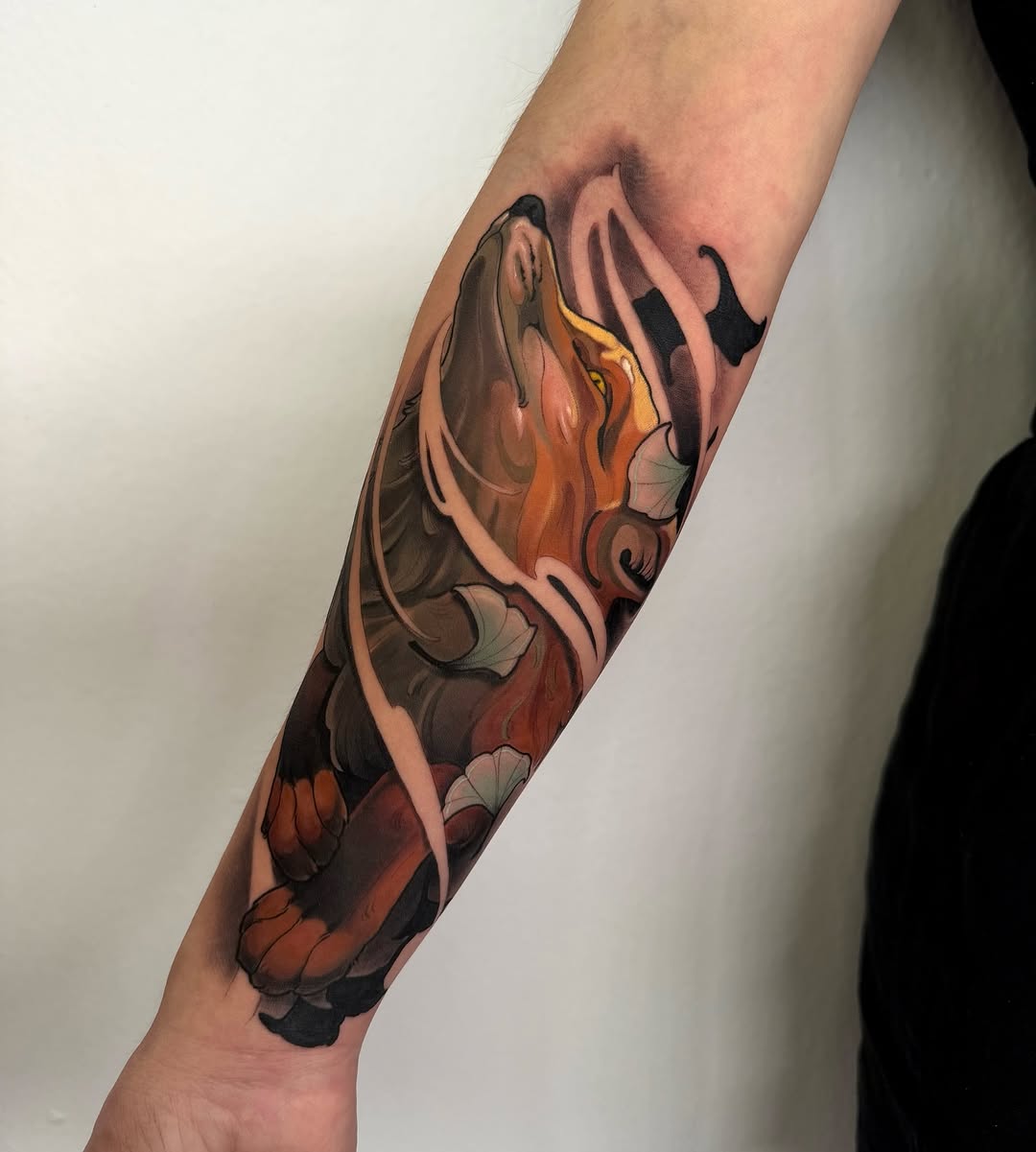 Colorful koi fish tattoo on a forearm featuring orange, yellow, black, and cream tones with detailed scales and fins.