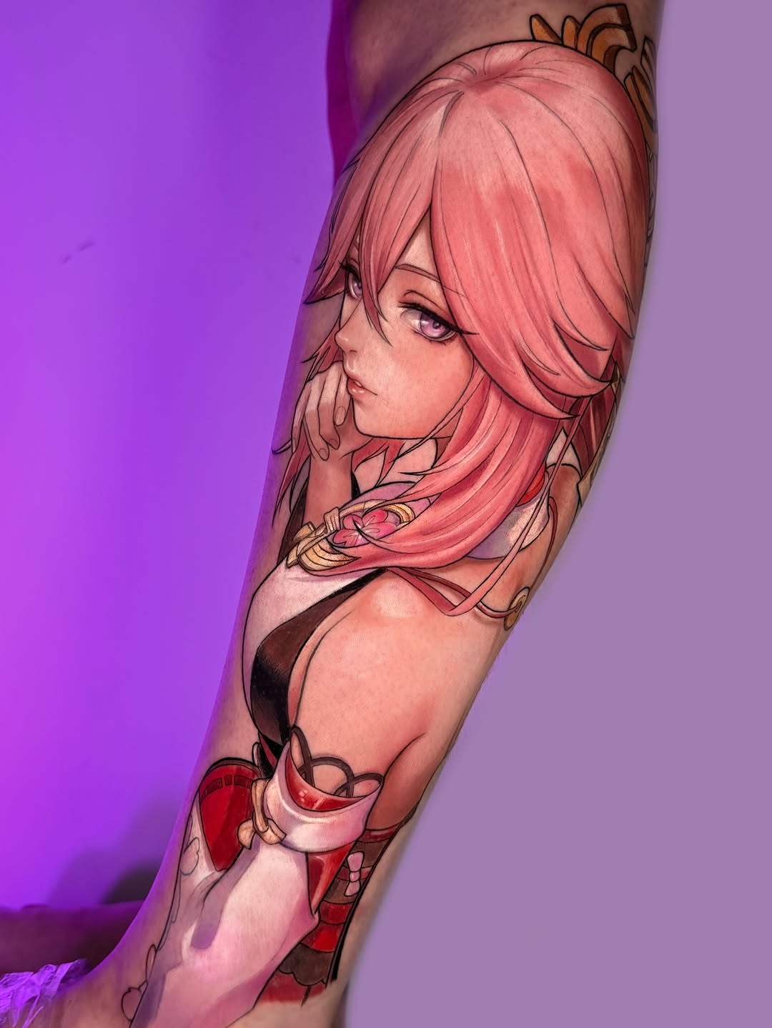 Colorful arm tattoo featuring a pink-haired female character with gold ornamental details and red clothing elements against a purple background.