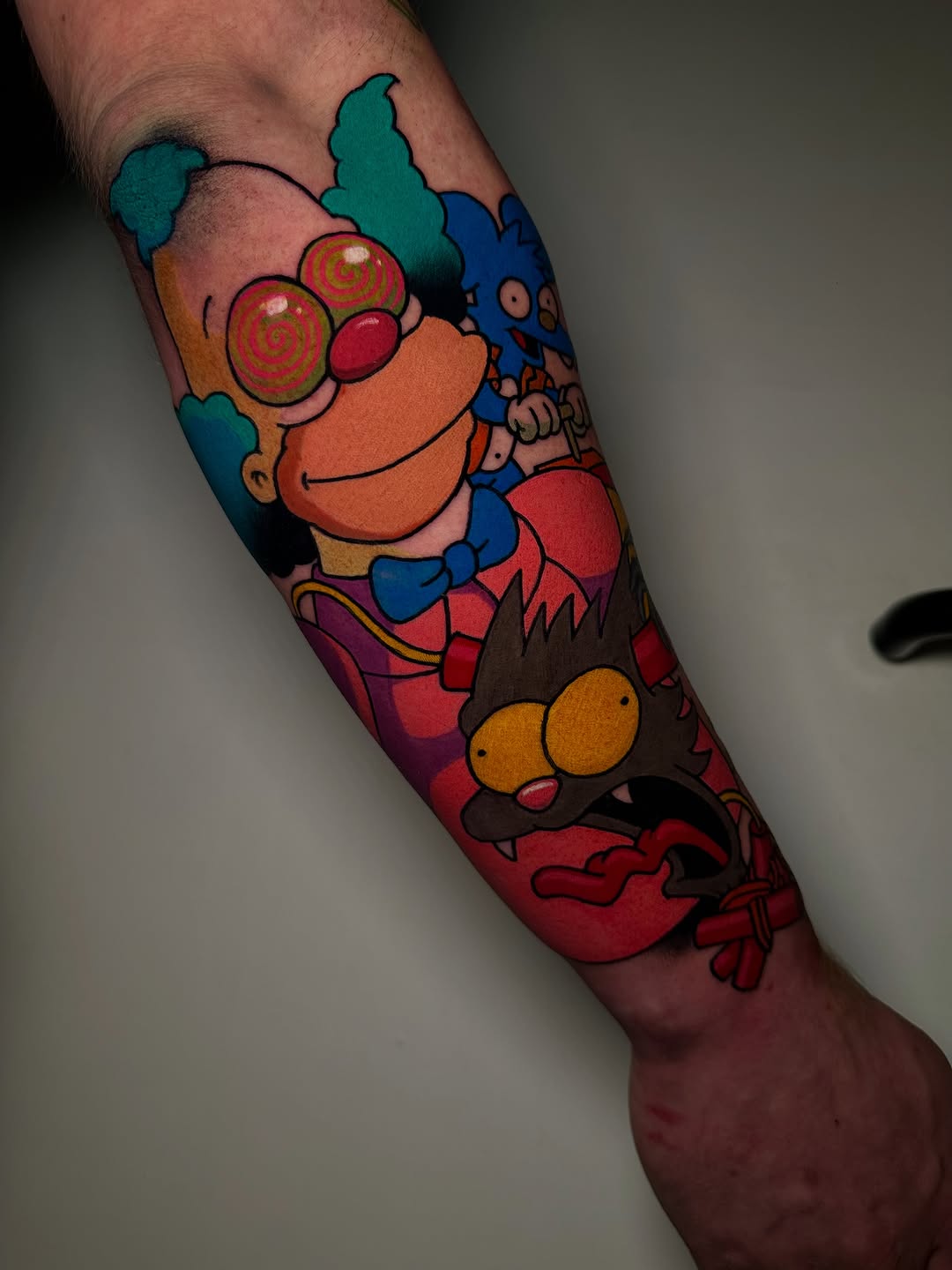 Colorful cartoon characters with spiral eyes and expressive faces tattooed on the forearm and calf, featuring vibrant reds, blues, oranges, and teals.