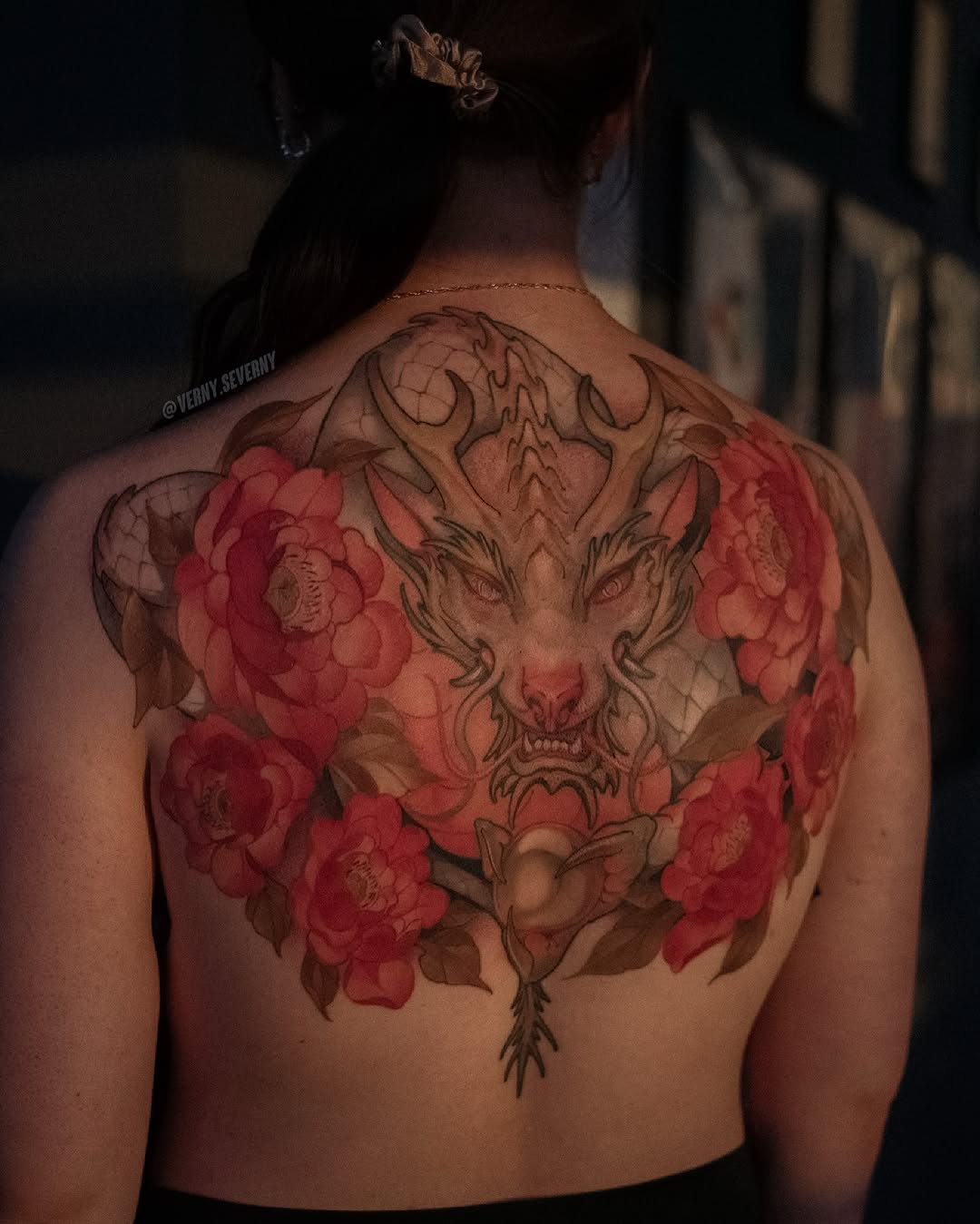 Back tattoo featuring a demonic horned face surrounded by red roses with brown linework and shading on bare skin.