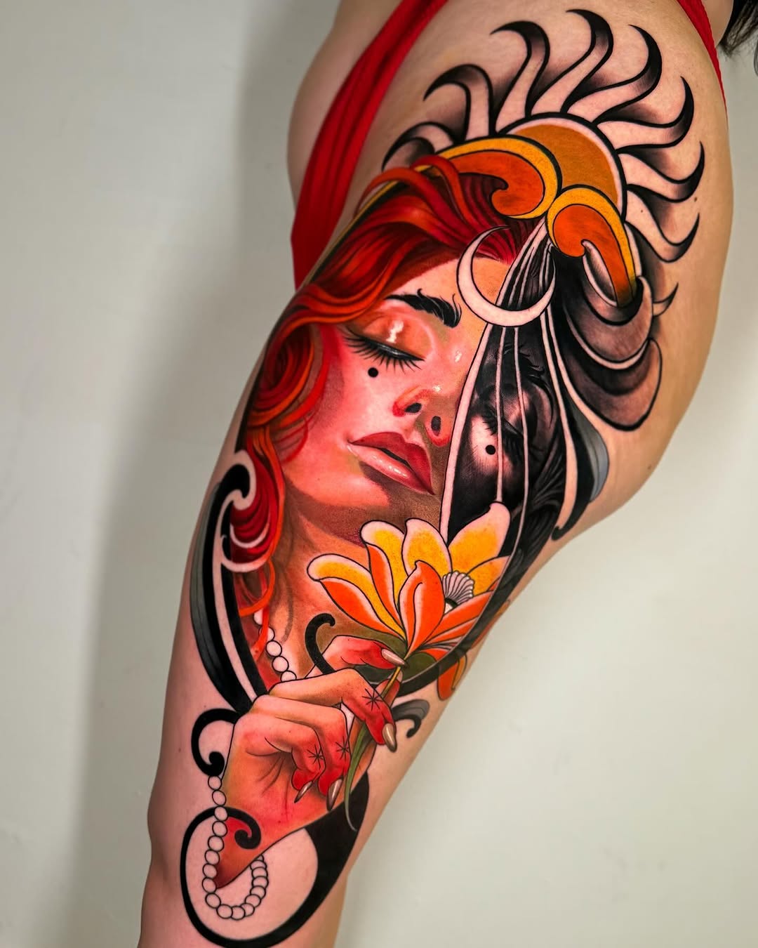 Colorful tattoo on upper arm featuring a woman's face with red hair, ornamental headdress, flower, and decorative black swirls in orange, red, and black tones.