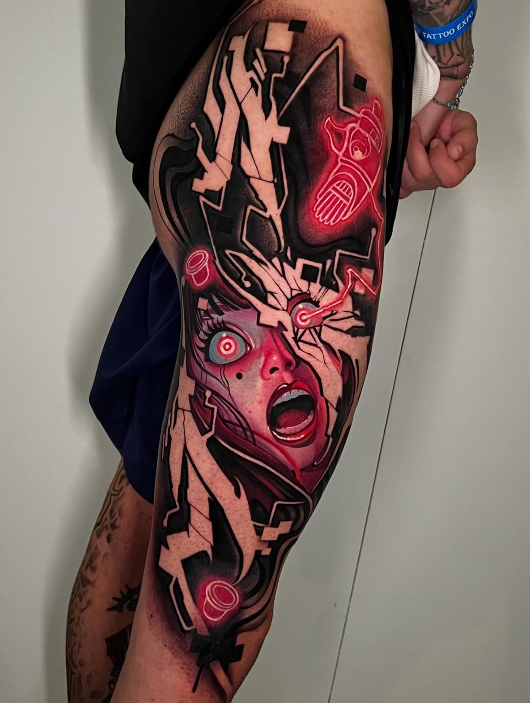 Vibrant leg tattoo featuring an expressive face with wide eyes and open mouth, geometric shapes, and glowing red neon elements throughout the design.