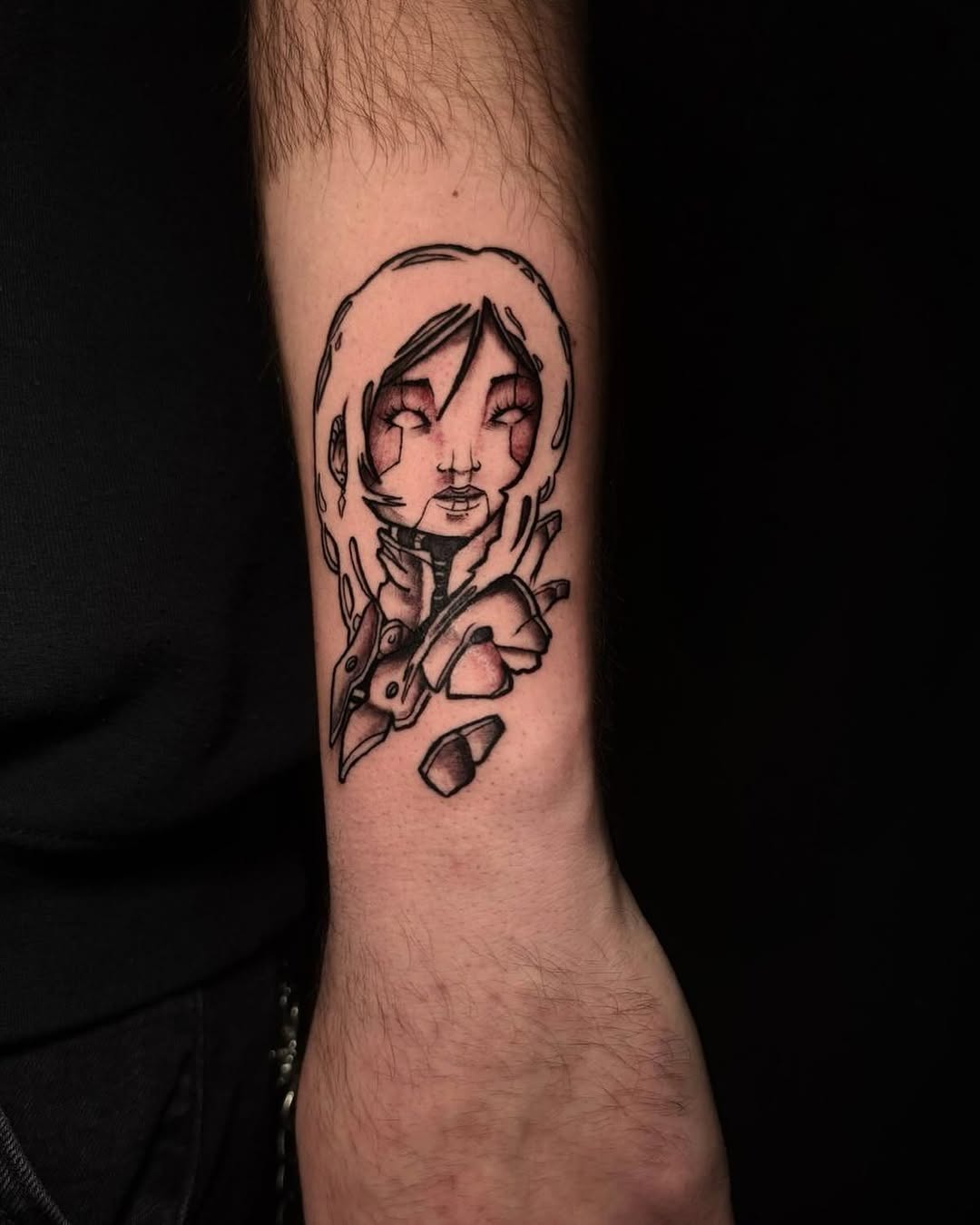 Monochromatic portrait tattoo of a person with closed eyes and shoulder-length hair, adorned with ornamental neck piece and scattered geometric shapes, positioned on the forearm.
