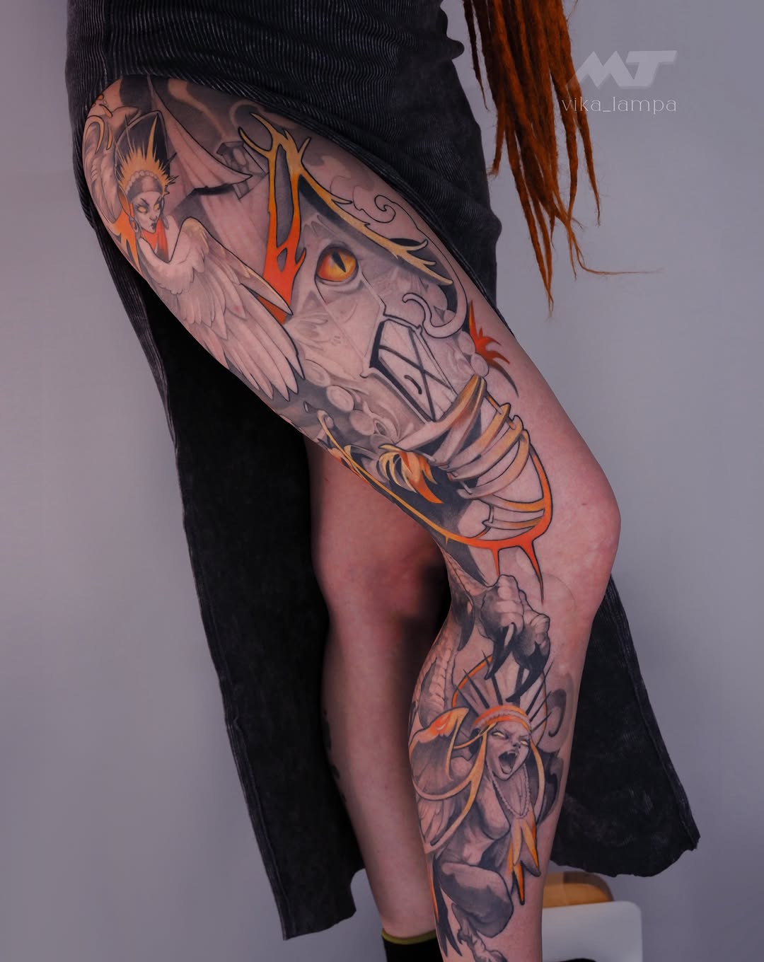 Colorful leg tattoo featuring a skull with wings, angelic figures, and ornamental details in orange, gold, and grey tones on the thigh and calf.