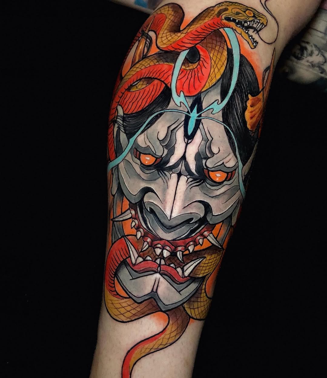 Colorful leg tattoo featuring intertwined serpents in red and gold with a gray demon mask, turquoise accents, and ornamental details on the thigh and calf.