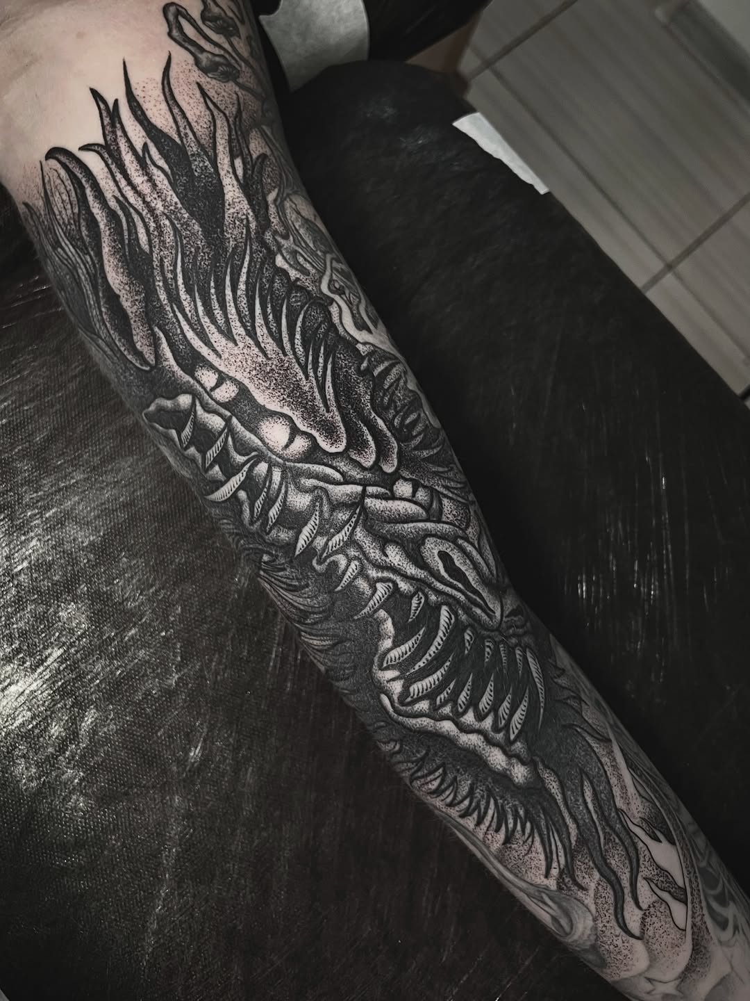 Detailed wing and feather tattoo covering the forearm with intricate linework and shading in black ink on pale skin.