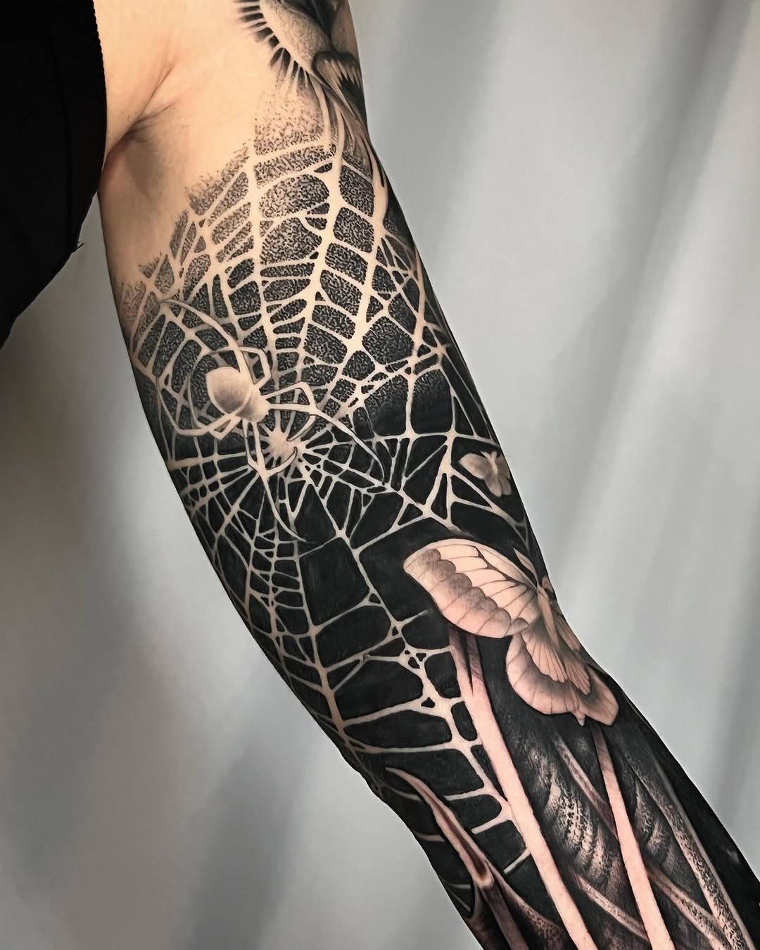 Intricate spider web and spiders tattoo on forearm with detailed shading, negative space details, and flesh-tone accents on black background.
