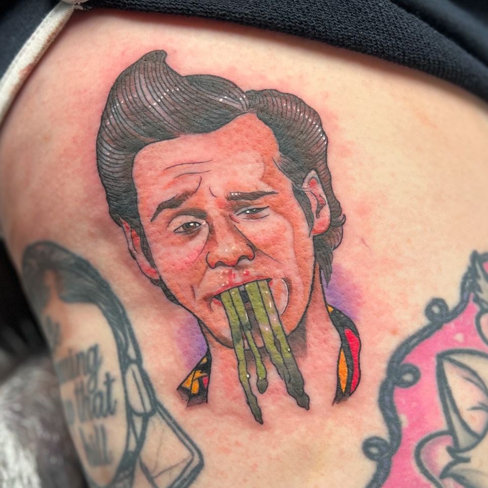 Colored shoulder tattoo depicting a man's face with dark hair and open mouth, featuring green tentacles or strands emerging from his mouth, with red and yellow accents.
