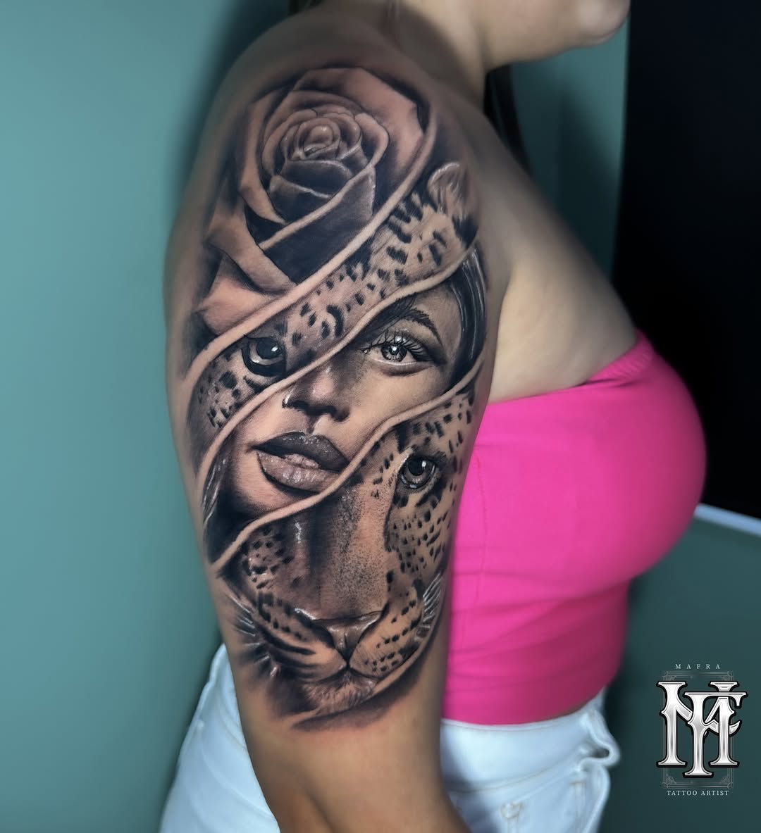 Shoulder tattoo featuring a woman's face with a rose and leopard head intertwined with ribbon wraps, rendered in grayscale on skin.