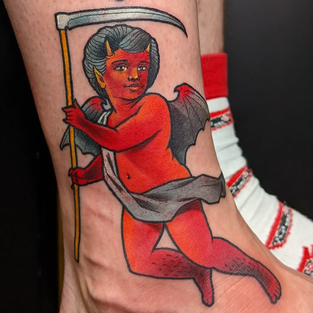 Red demon child figure holding a scythe with gray hair and wings, tattooed on the leg with black outlines and red, orange, and gray coloring.