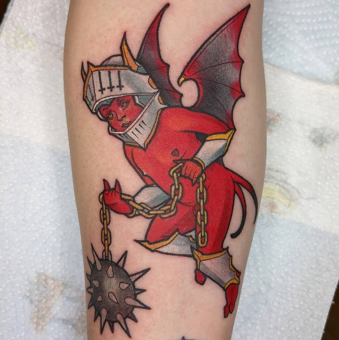 Red demon figure with horns, white facial markings, and chains tattooed on a calf, featuring gold accents and a spiked ball detail.