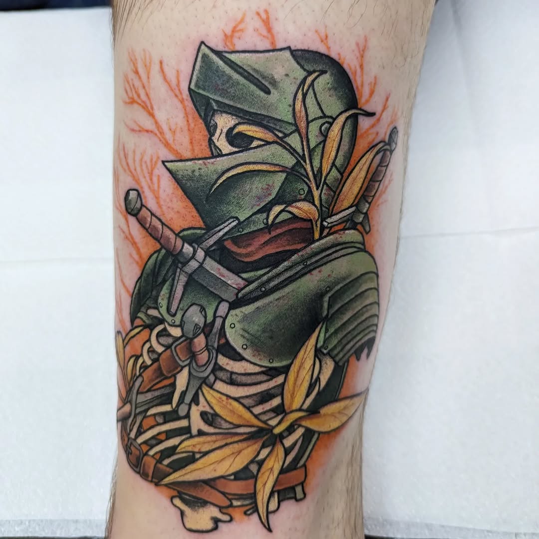 Colored tattoo on a leg showing a masked ninja warrior in green armor wielding a sword, surrounded by orange foliage and yellow leaves.